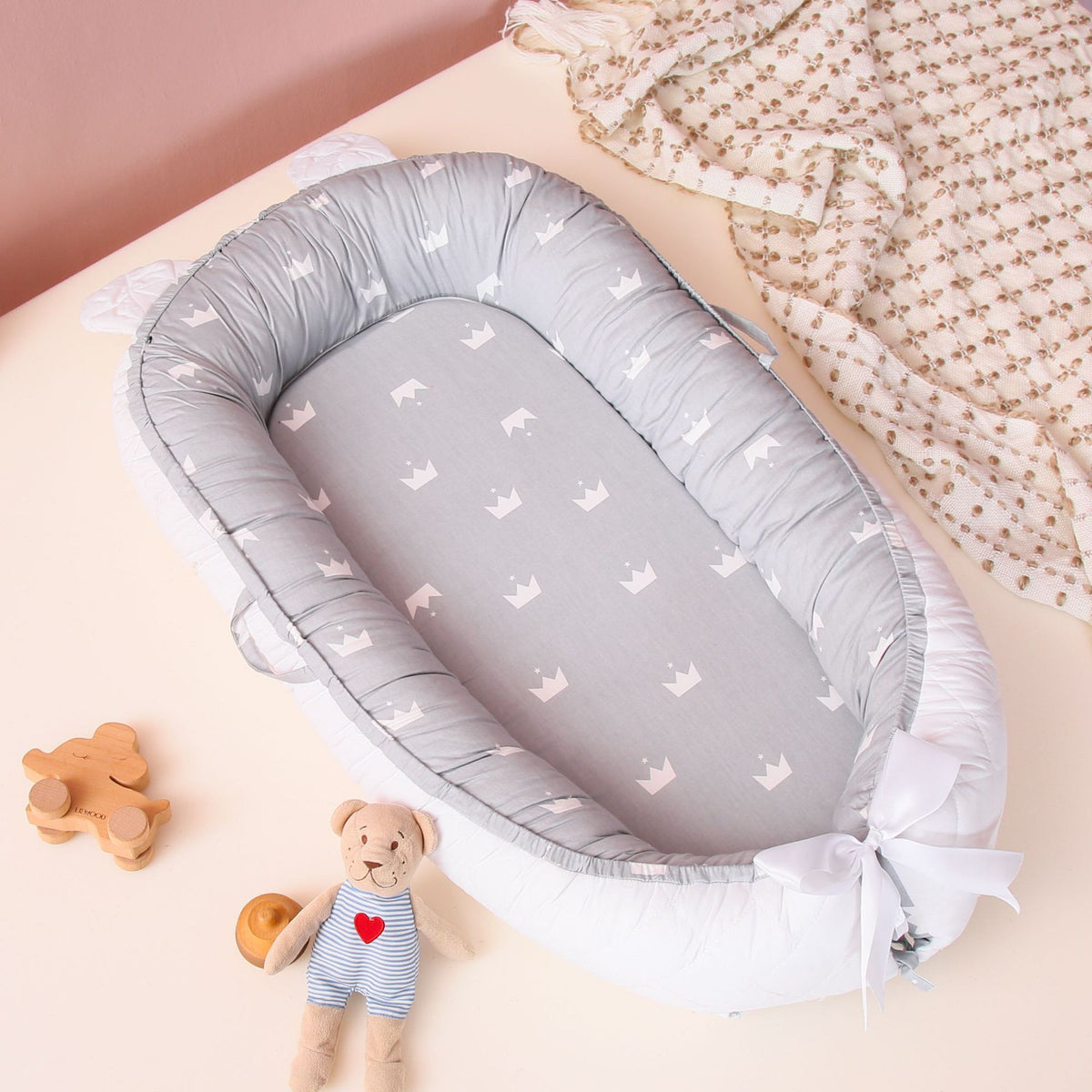 A gray and white Cuddle Newborn Baby Lounger with soft edges, placed on a table with a plush toy and a blanket in the background.